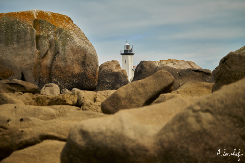 Un phare émerge de derrière les rochers, sur la côte bretonne