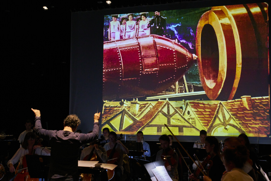 Benjamin Levy dirige l’Orchestre National de Cannes en ciné-concert dans la partition d’Alexis Savelief sur le film de Georges Méliès “Le Voyage dans la Lune”, ici la scène où la capsule spatiale est insérée dans le canon…