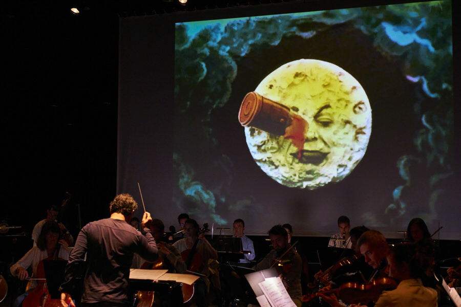 Benjamin Levy dirige l’Orchestre National de Cannes en ciné-concert dans la partition d’Alexis Savelief sur le film de Georges Méliès “Le Voyage dans la Lune”, ici la fameuse image où la Lune reçoit la capsule spatiale dans l’œil…